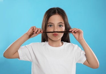 Photo of Cute little girl making fake mustache with her hair on turquoise background