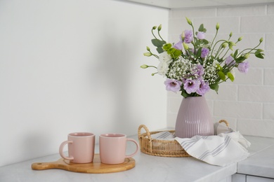 Beautiful bouquet with Eustoma flowers and cups on table indoors