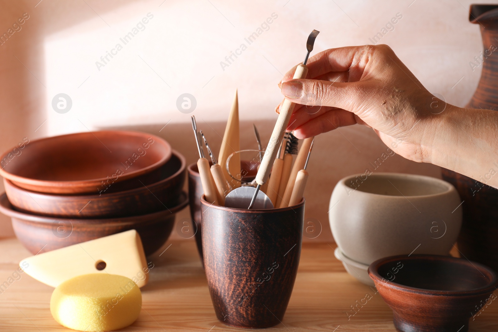 Photo of Woman taking clay crafting tool from cup in workshop, closeup