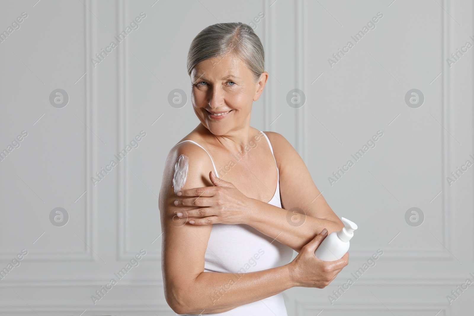 Photo of Happy woman applying body cream on shoulder near white wall