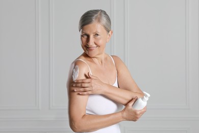 Photo of Happy woman applying body cream on shoulder near white wall