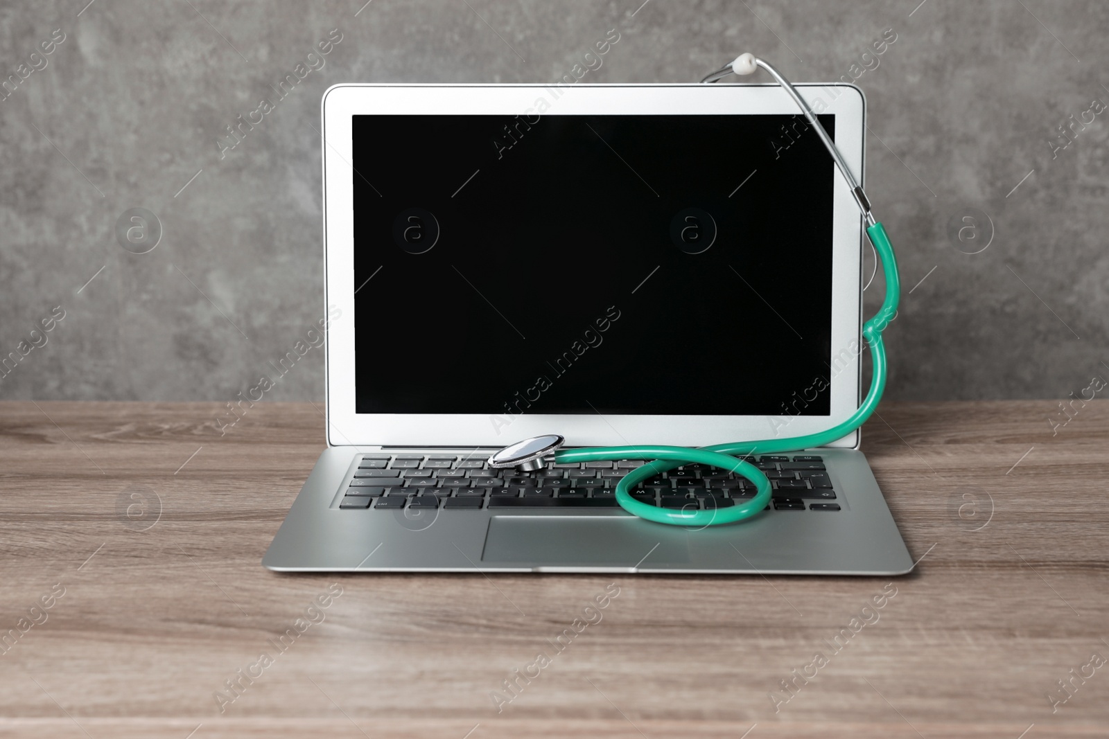 Photo of Laptop with blank screen and stethoscope on table against grey background. Computer repair