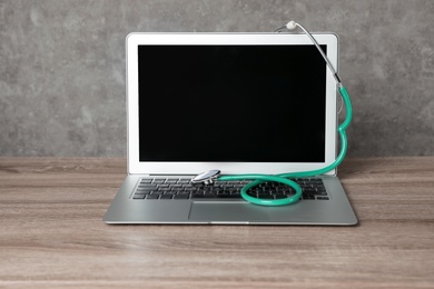 Laptop with blank screen and stethoscope on table against grey background. Computer repair