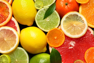 Photo of Sliced and whole citrus fruits with leaves as background, top view