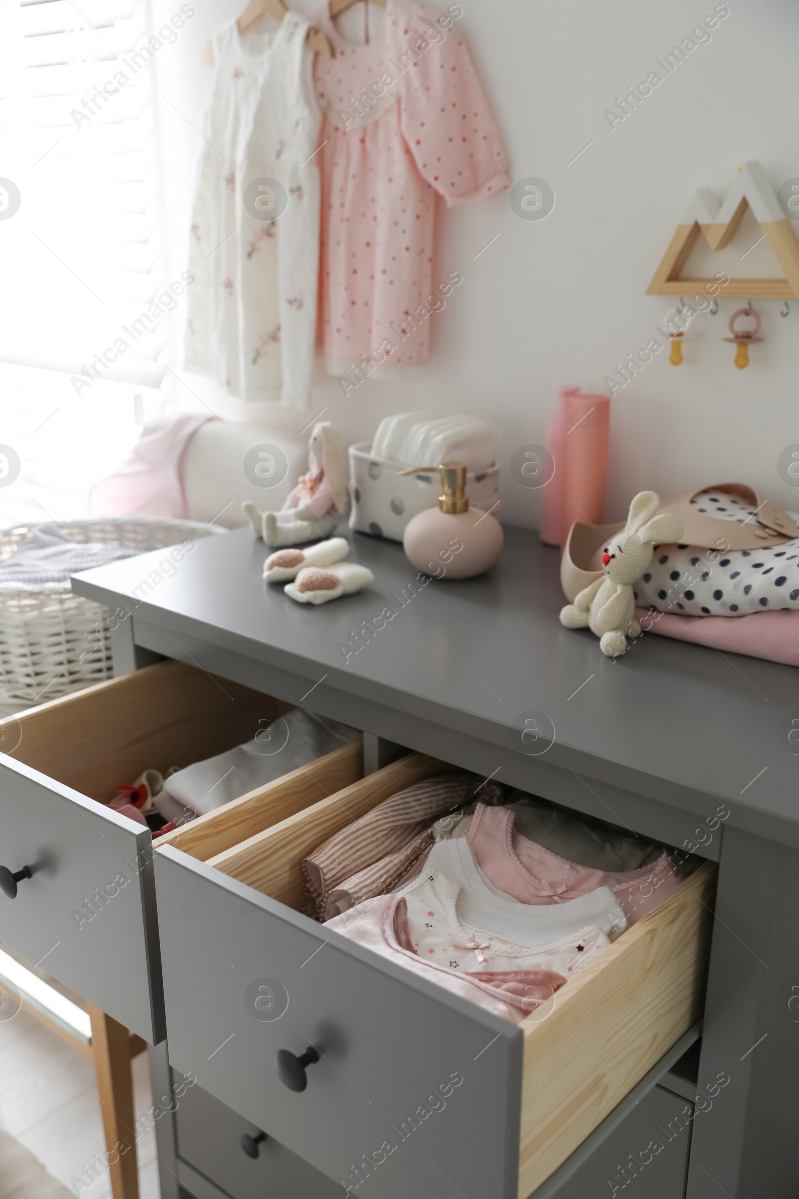 Photo of Open cabinet drawers with baby clothes and shoes in child room