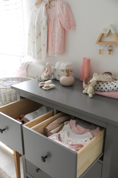 Open cabinet drawers with baby clothes and shoes in child room