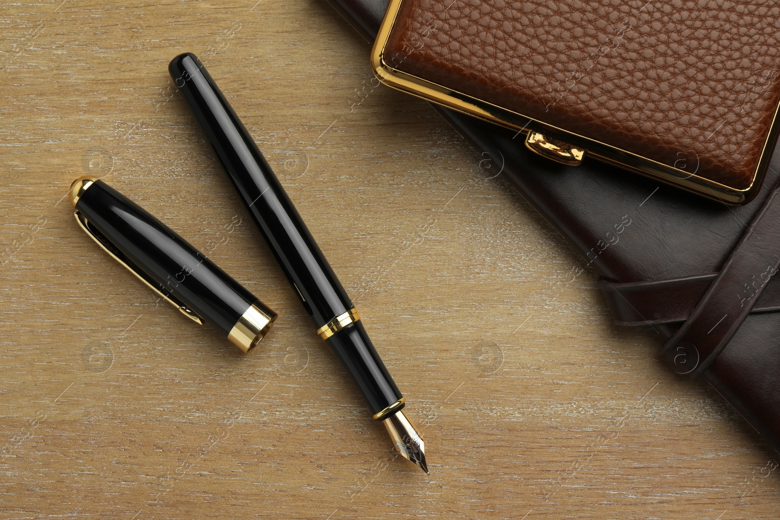 Photo of Stylish fountain pen, notebook and cigarette case on wooden table, flat lay