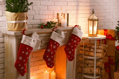 Red Christmas stockings with gifts on decorative fireplace in festive room interior