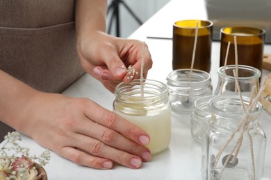 Photo of Woman decorating homemade candle with gypsophila flowers at table indoors, closeup