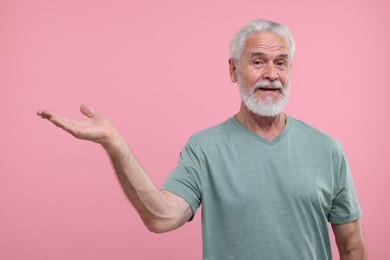 Special promotion. Senior man holding something on pink background. Space for text