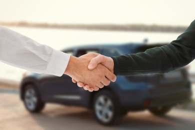 Image of Man buying car and shaking hands with salesman against blurred auto, closeup