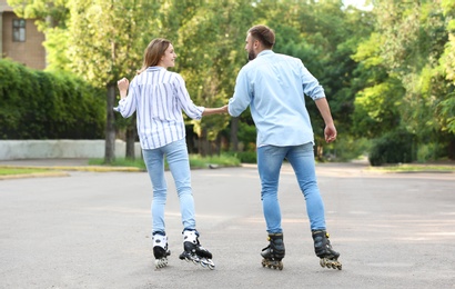Photo of Young couple roller skating on city street, back view