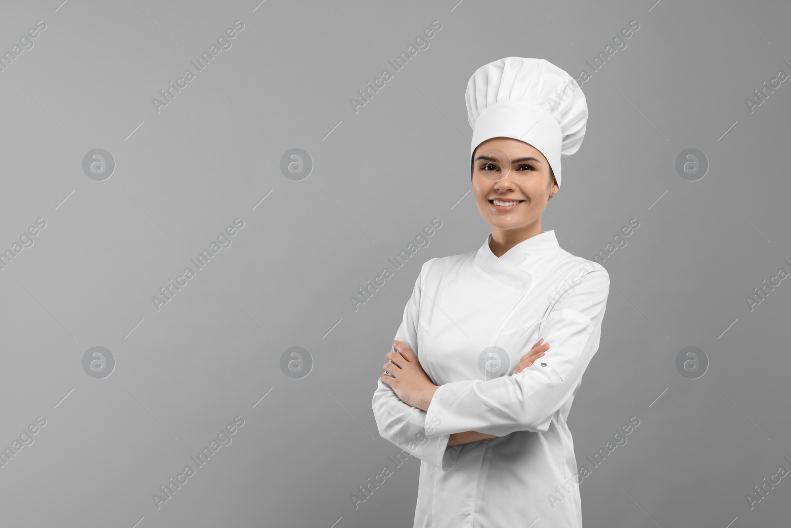 Photo of Happy female chef wearing uniform and cap on light grey background. Space for text