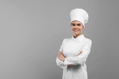 Happy female chef wearing uniform and cap on light grey background. Space for text
