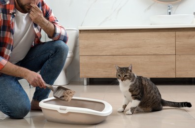 Photo of Young man cleaning cat litter tray in bathroom