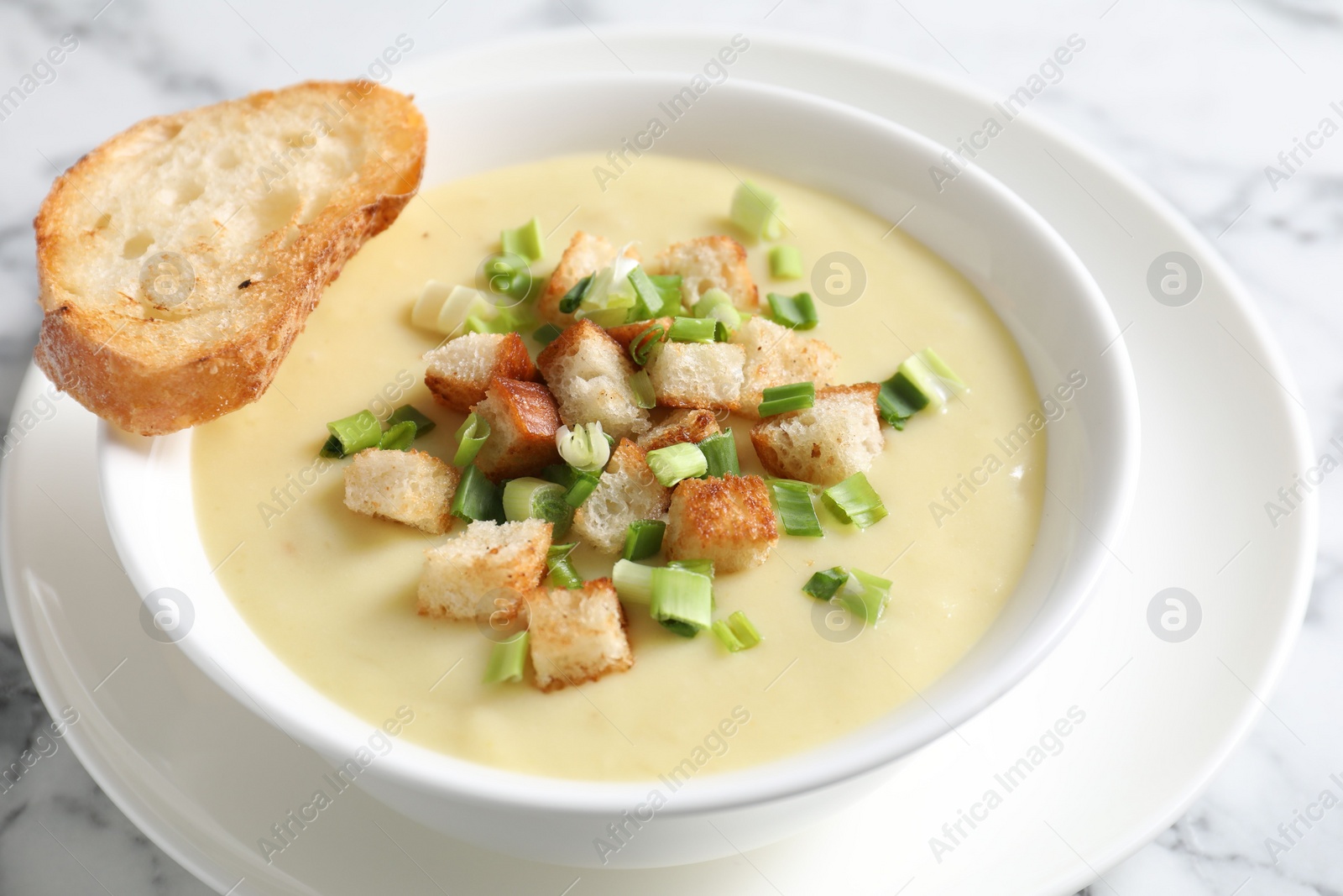 Photo of Tasty potato soup with croutons and green onion in bowl on white marble table