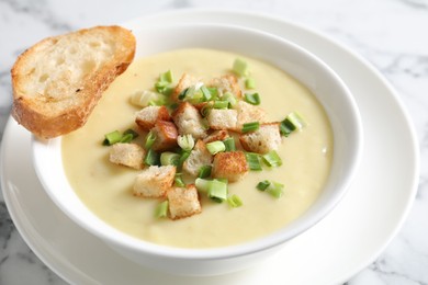 Photo of Tasty potato soup with croutons and green onion in bowl on white marble table