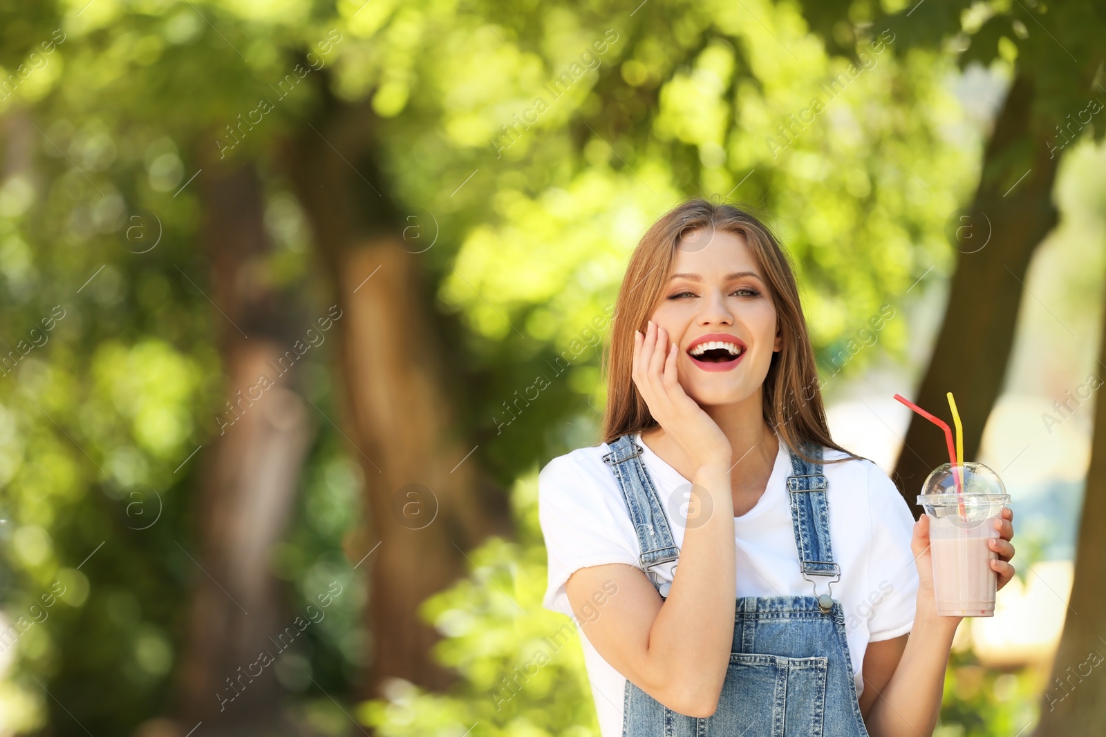 Photo of Young woman with cup of delicious milk shake outdoors