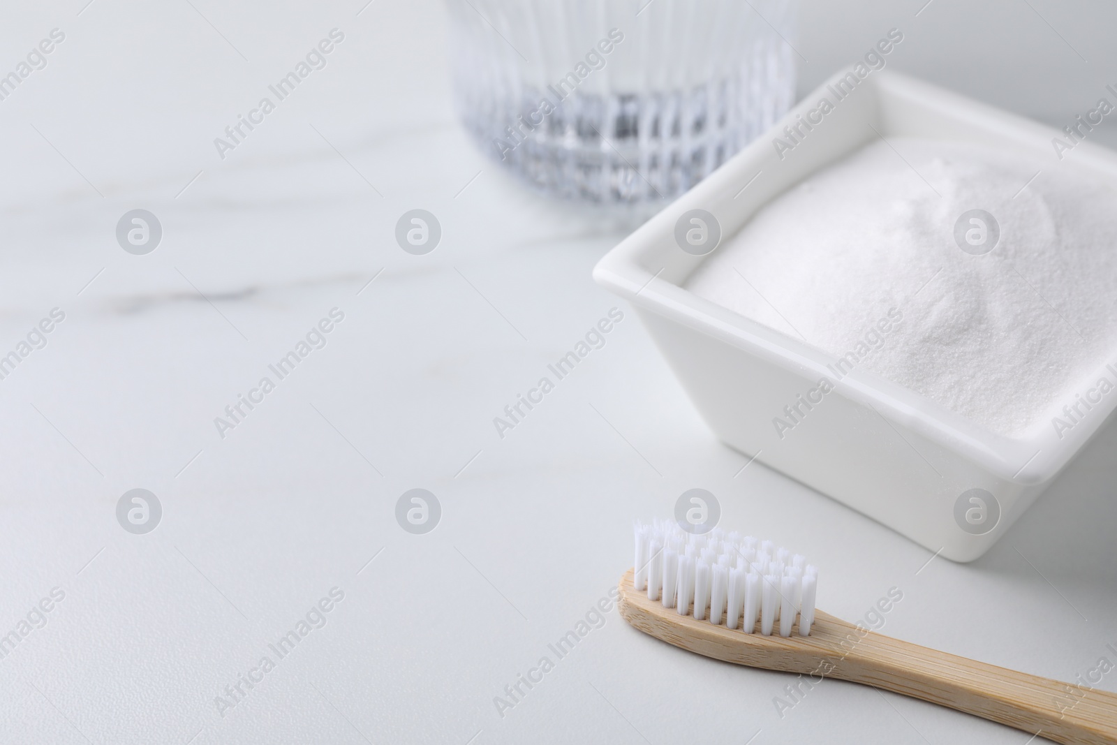 Photo of Bamboo toothbrush and bowl of baking soda on white table, closeup. Space for text