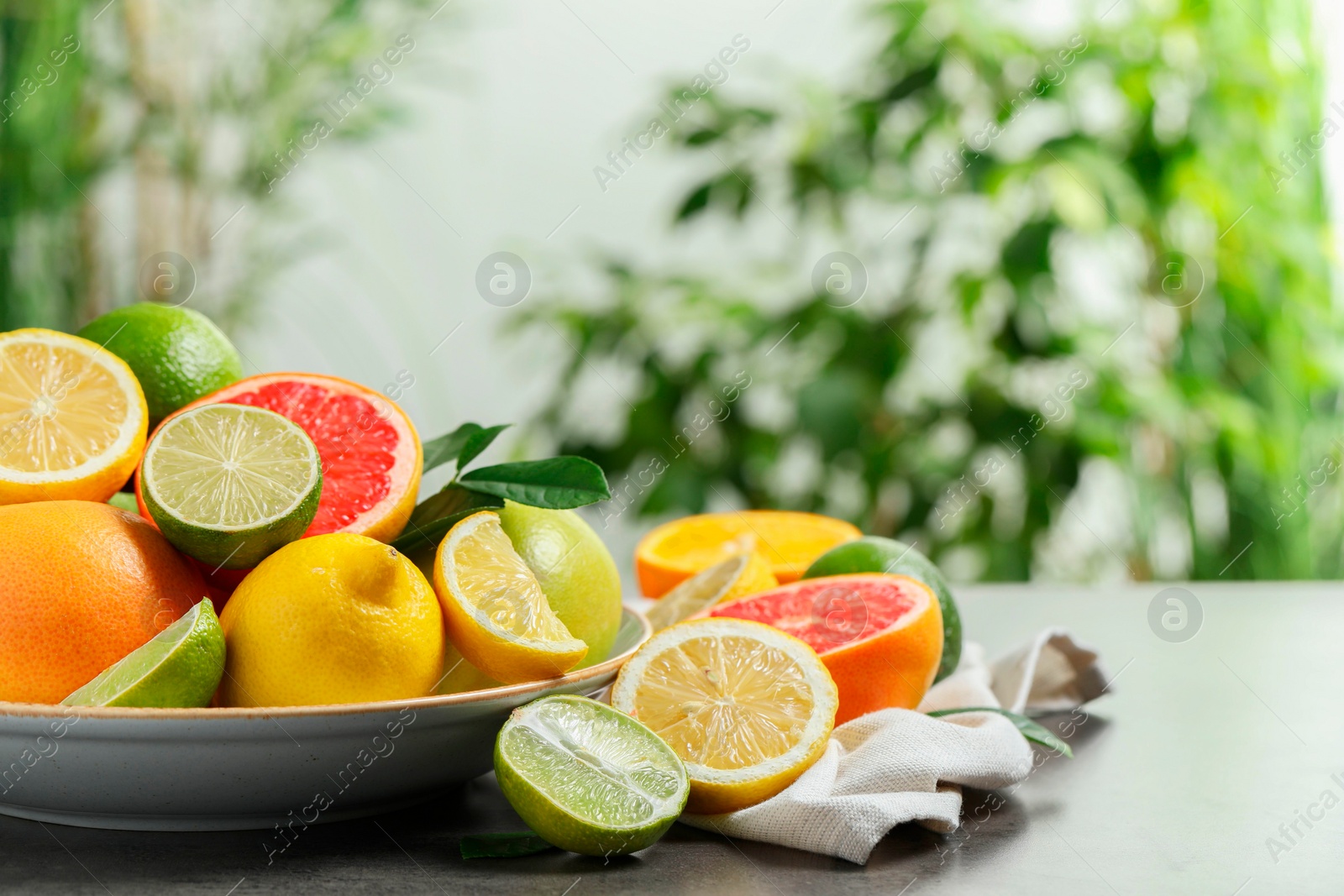 Photo of Different fresh citrus fruits on grey table against blurred background, closeup. Space for text