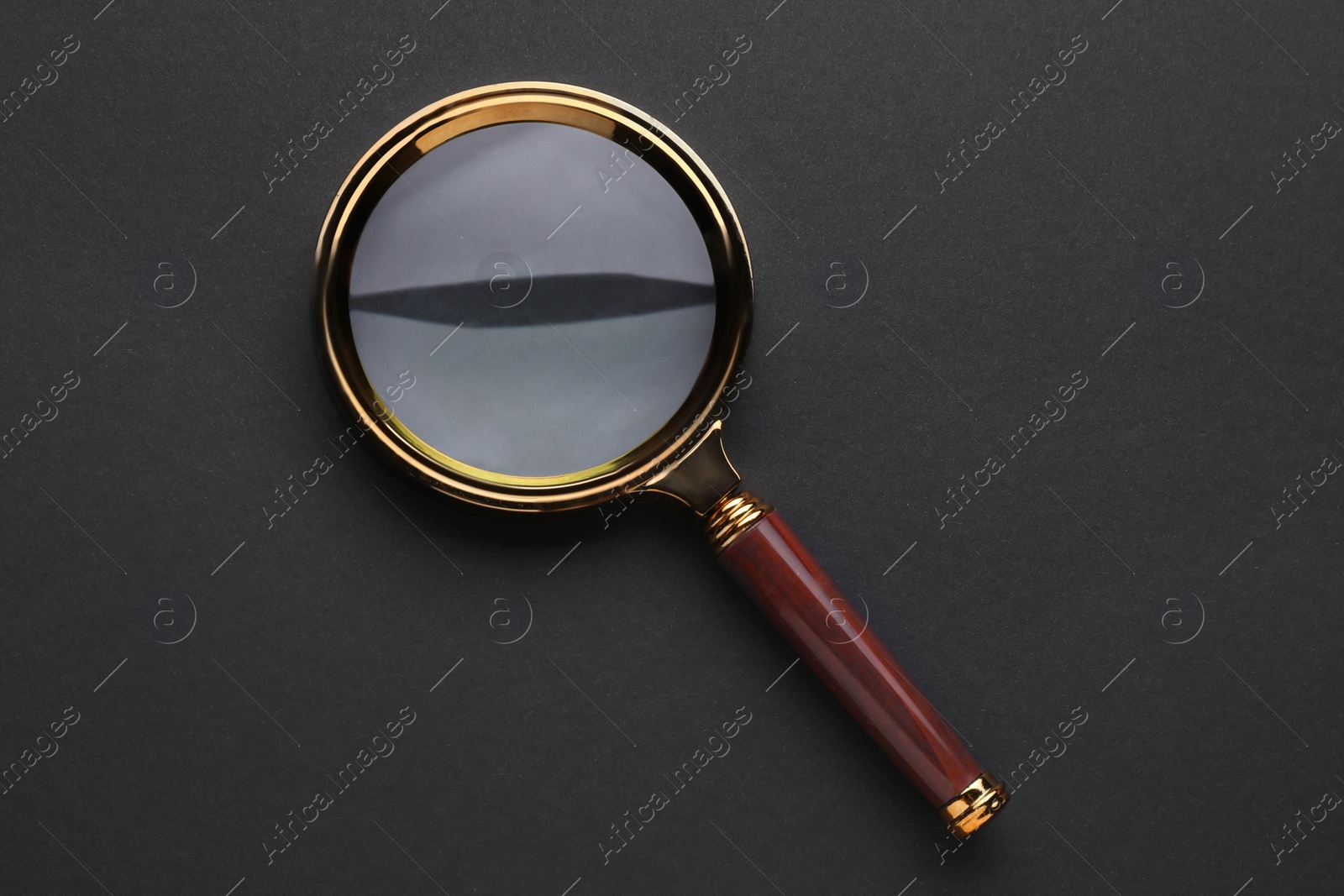 Photo of Magnifying glass on dark background, top view