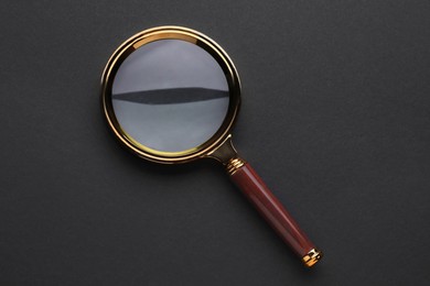 Photo of Magnifying glass on dark background, top view