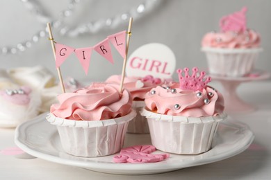 Photo of Delicious cupcakes with pink cream and toppers for baby shower on white wooden table