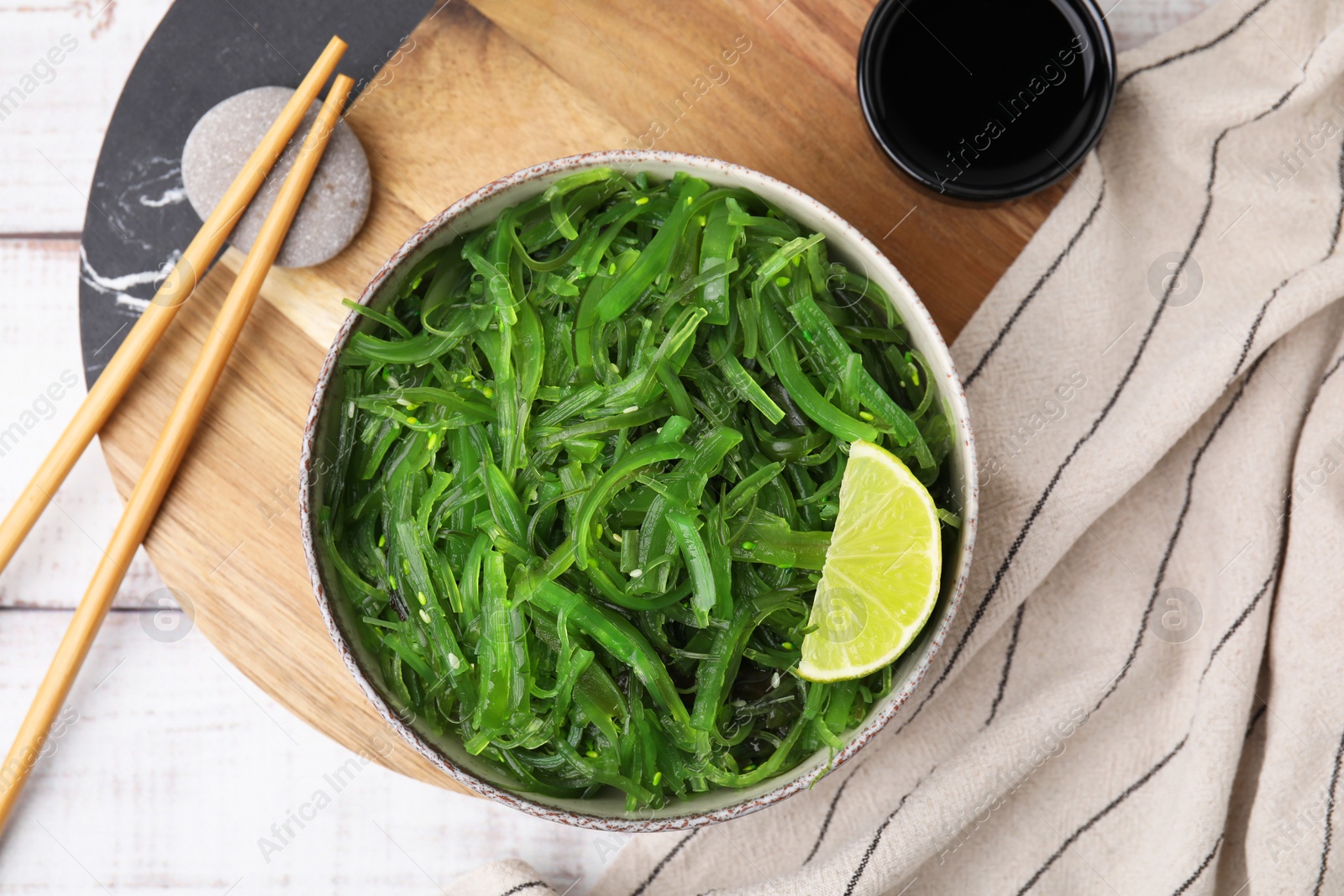 Photo of Tasty seaweed salad in bowl served on wooden table, flat lay