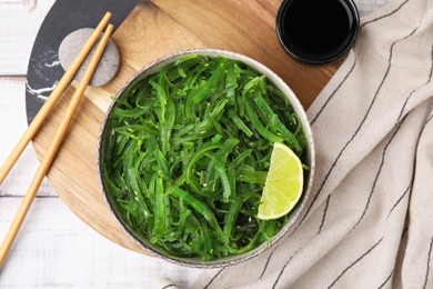 Tasty seaweed salad in bowl served on wooden table, flat lay