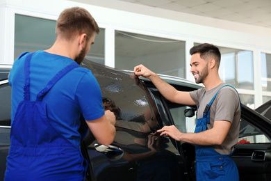 Photo of Workers tinting car window with foil in workshop