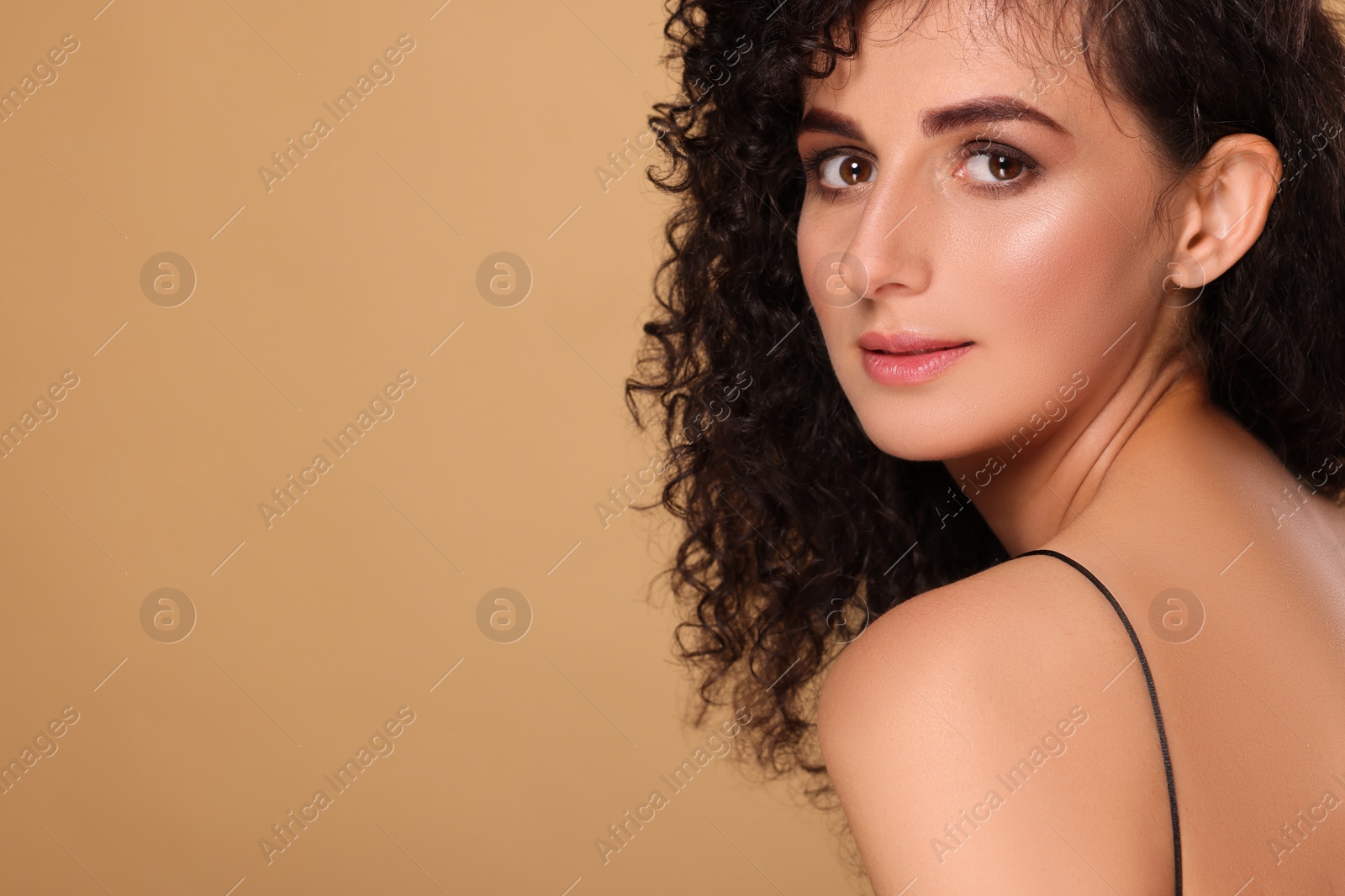 Photo of Beautiful young woman with long curly hair on beige background. Space for text