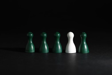 Photo of Choice concept. White pawn among green ones on black table