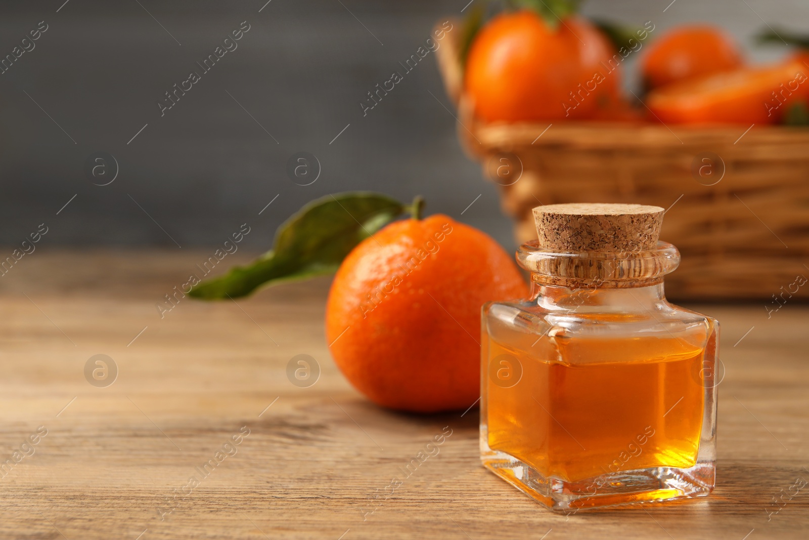 Photo of Bottle of tangerine essential oil and fresh fruit on wooden table, closeup. Space for text