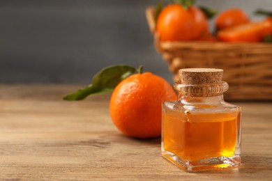 Bottle of tangerine essential oil and fresh fruit on wooden table, closeup. Space for text