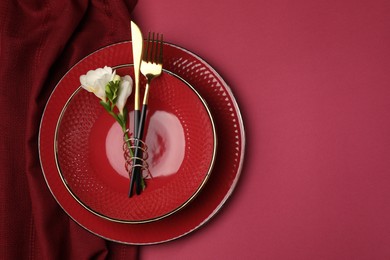 Photo of Stylish table setting with cutlery and floral decor on pink background, top view. Space for text