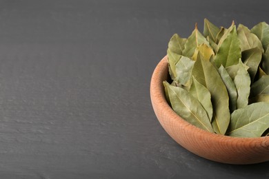 Photo of Aromatic bay leaves in wooden bowl on gray table, closeup. Space for text