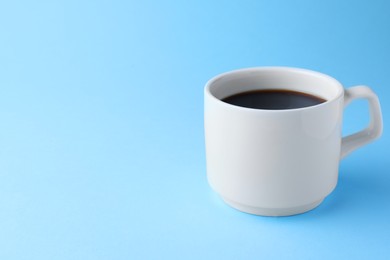 Photo of White mug of freshly brewed hot coffee on light blue background, space for text