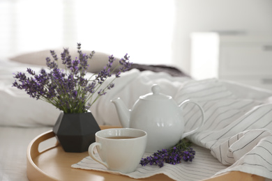 Wooden tray with cup of hot tea and beautiful lavender flowers on bed. Tasty breakfast