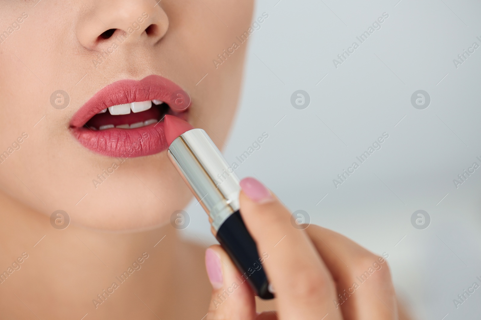 Photo of Young woman applying lipstick on light background, closeup