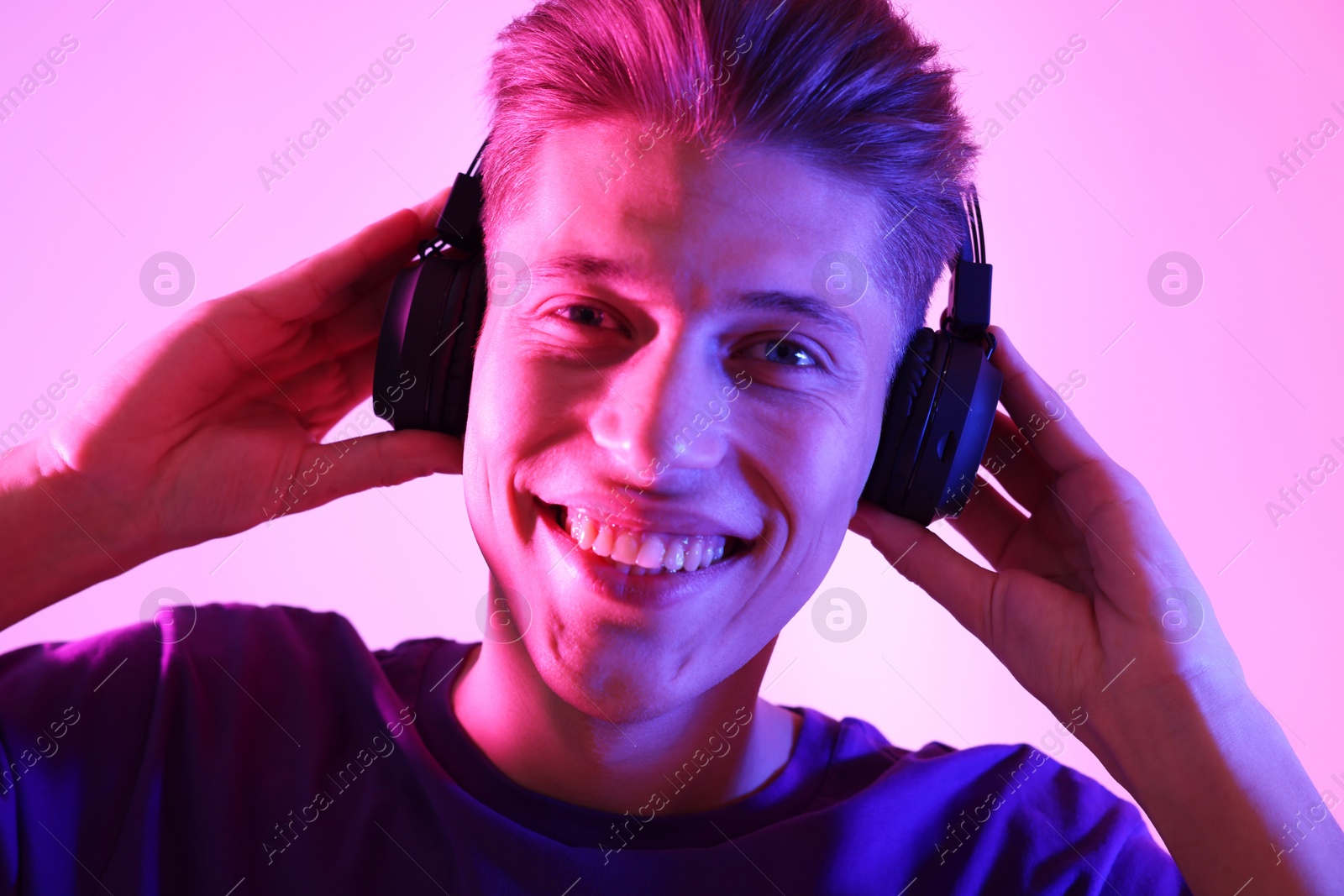 Photo of Young man with headphones on pink background in neon lights