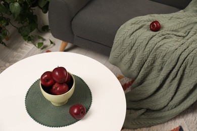 Photo of Red apples on coffee table near grey sofa with blanket indoors