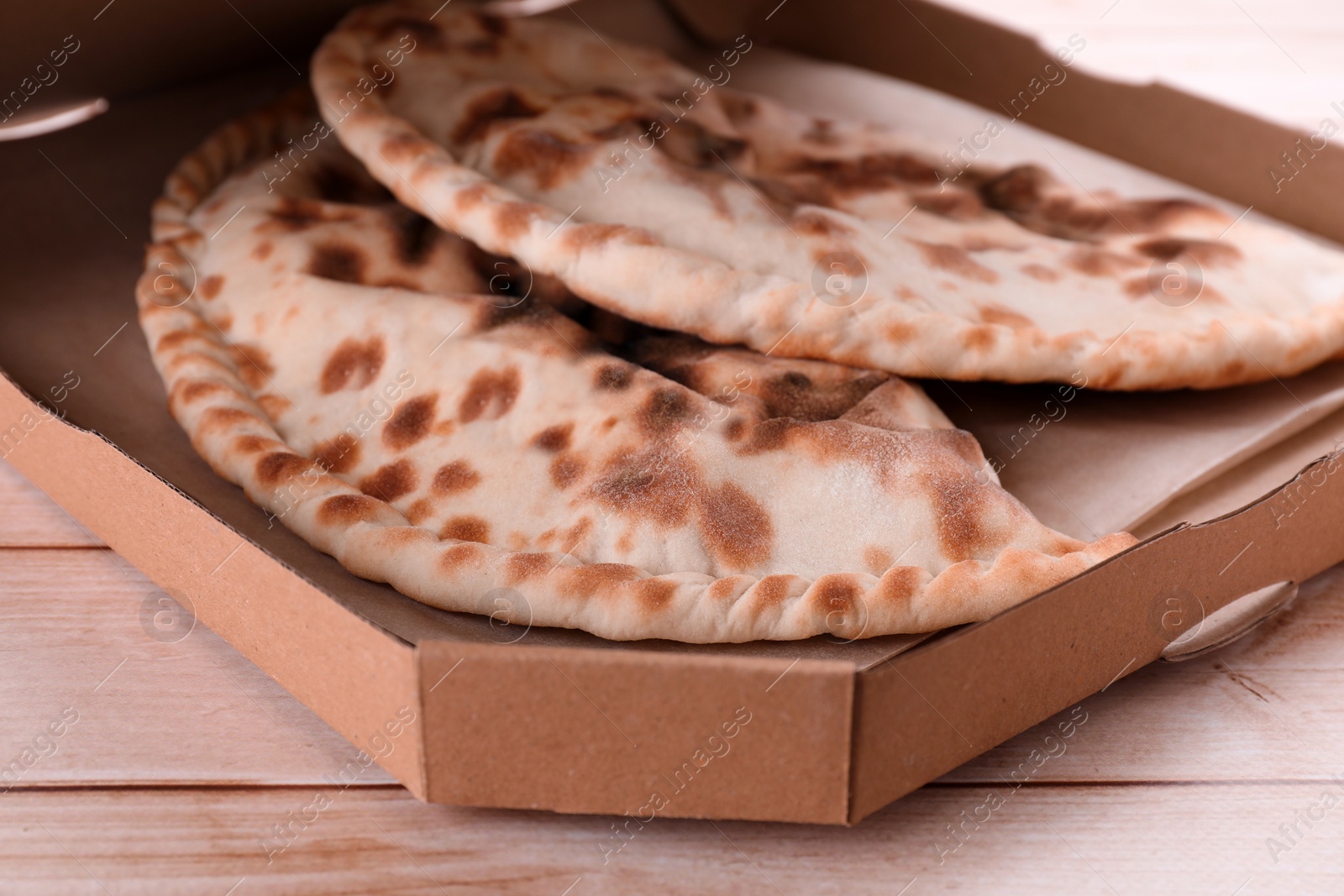 Photo of Cardboard box with delicious calzones on light wooden table, closeup