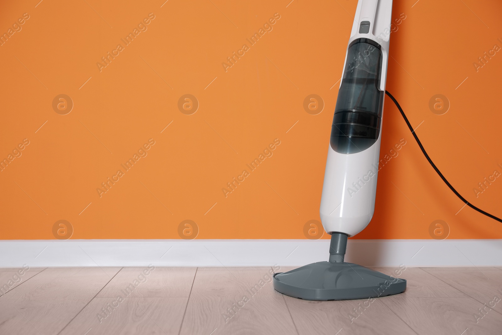Photo of One modern steam mop on floor near orange wall, space for text