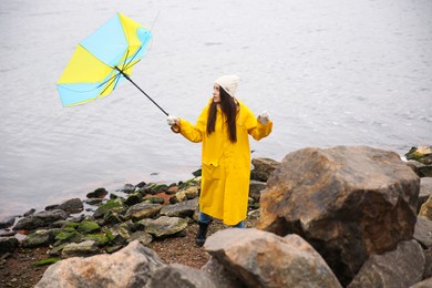 Woman in yellow raincoat with umbrella caught in gust of wind near river