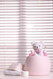 Photo of Wicker basket with baby cosmetic products and knitted toy bear on white table