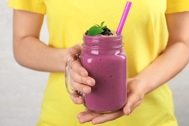 Young woman holding mason jar of tasty blackberry smoothie, closeup