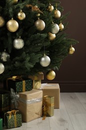 Photo of Beautifully decorated Christmas tree and many gift boxes near brown wall indoors, closeup