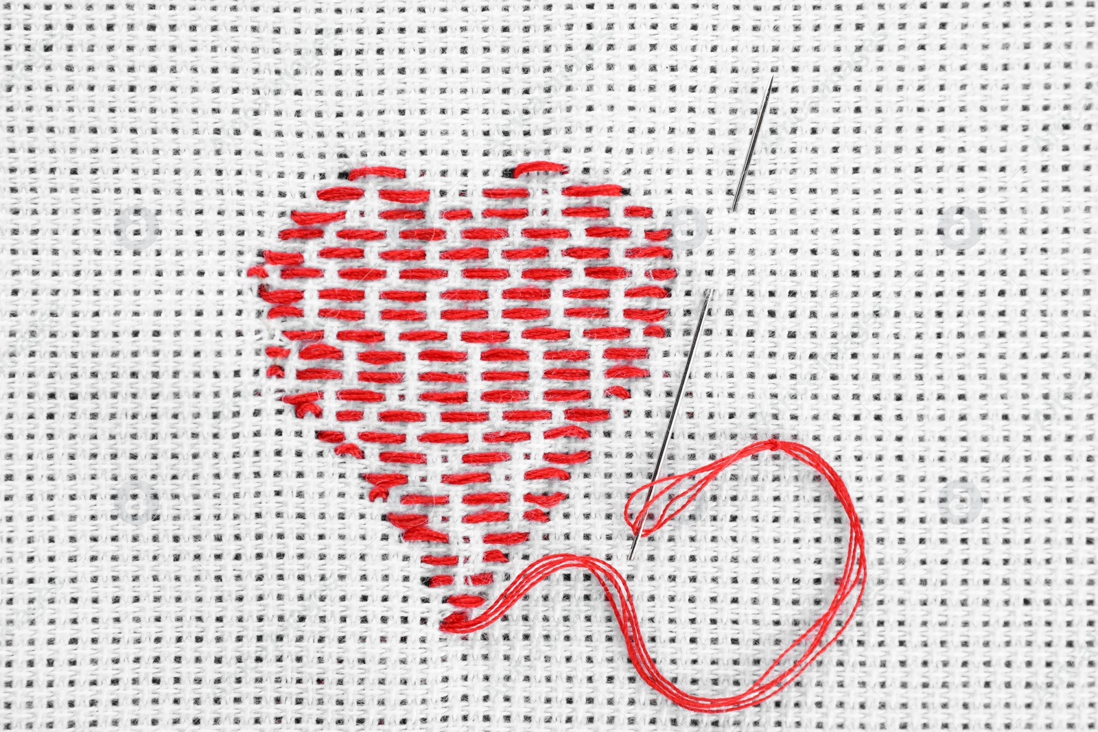 Photo of Canvas with embroidered heart and needle as background, top view