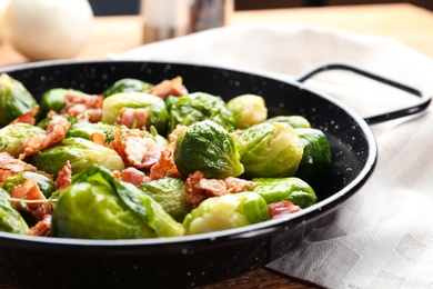 Photo of Tasty roasted Brussels sprouts with bacon on wooden table, closeup