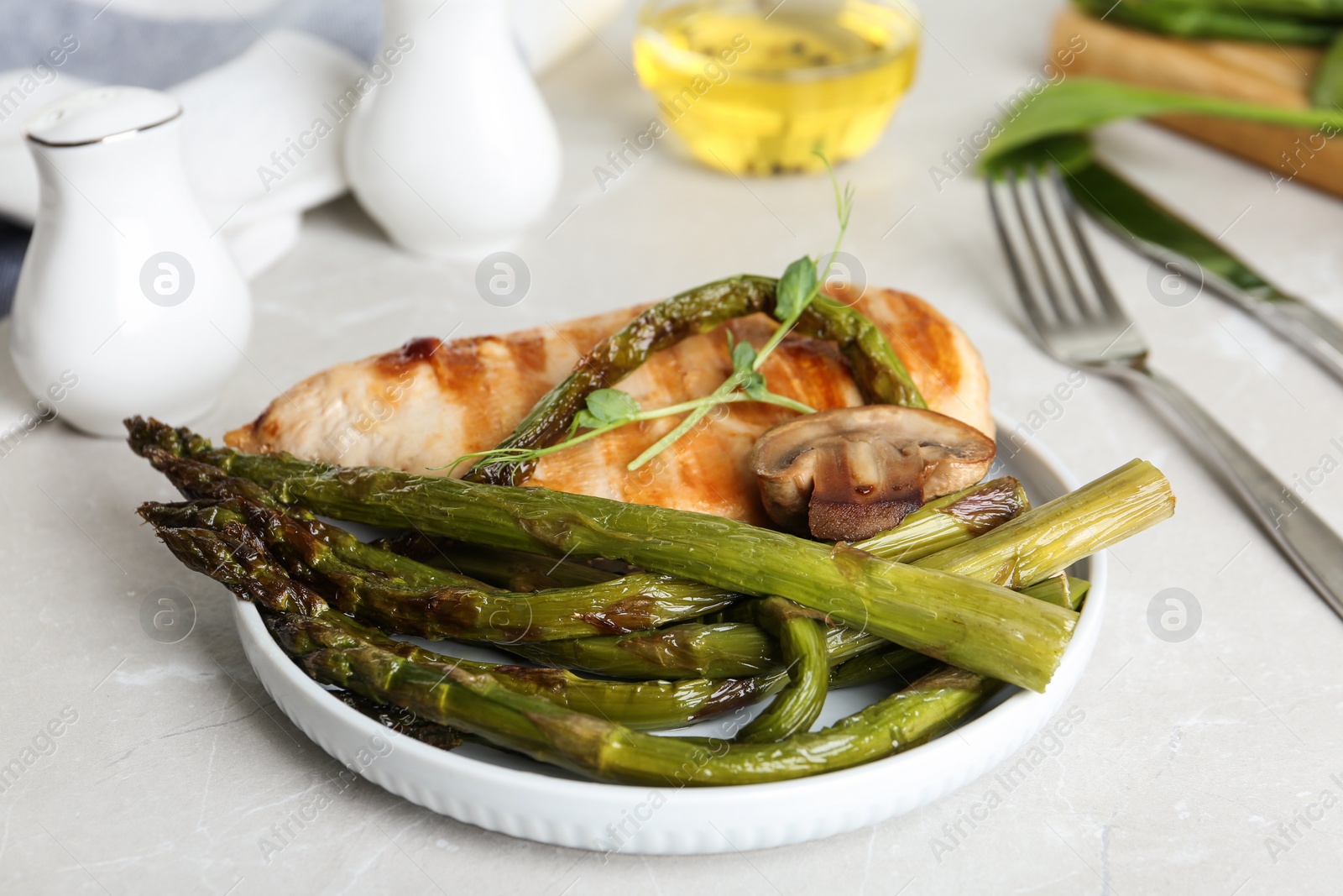 Photo of Tasty grilled chicken fillet served with asparagus on light grey marble table